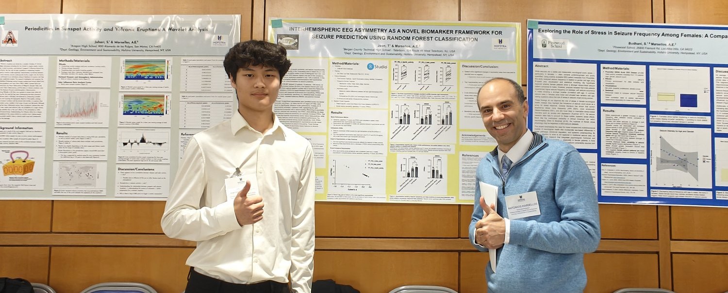 A high school researcher standing beside his printed poster at the Hofstra poster session, with Dr. Marsellos alongside